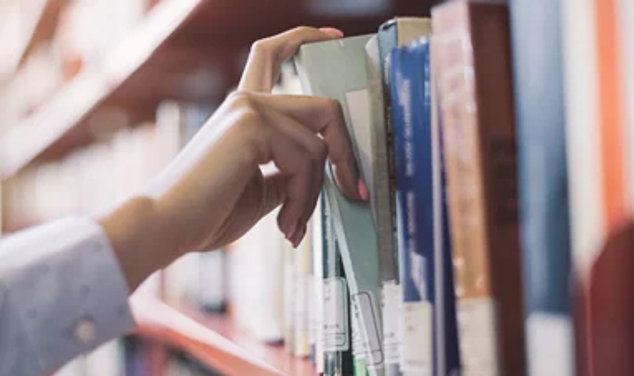 Hand tar ut en bok ur en bokhylla i ett bibliotek