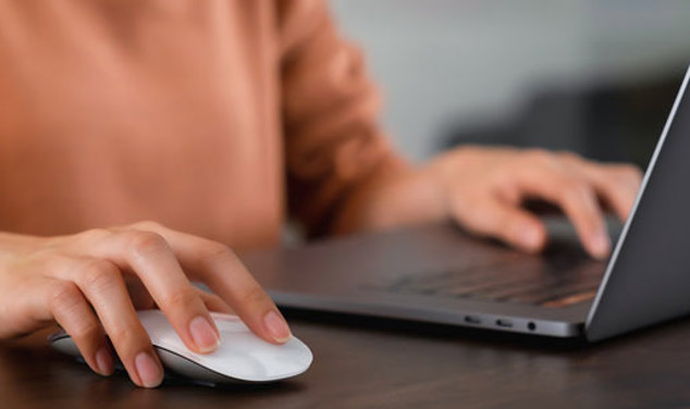 Person som klickar på en mus och skriver på en laptop.