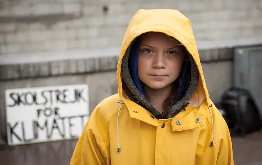 Greta Thunberg i gul regnkappa framfören skylt där det står Skolstrejk för klimatet