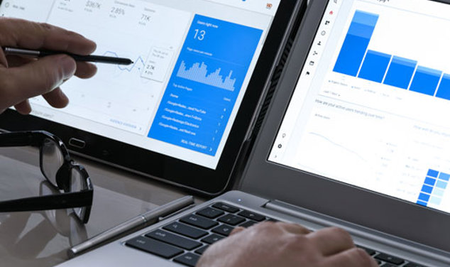 Någon tittar på Google Anaytics på två skärmar och pekar med en penna