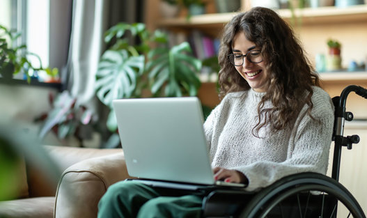 Ung kvinna i rullstol läser om tillgänglighet på laptop