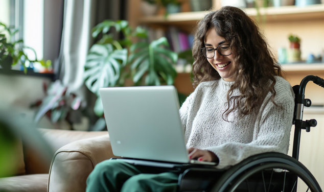 Ung kvinna i rullstol läser om tillgänglighet på laptop