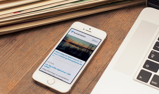 Bredvid en laptop ligger en mobiltelefon som visar en hemsida på skärmen.