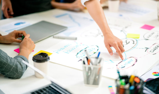 Personer samarbetar kring ett bord och pekar på en flowchart.